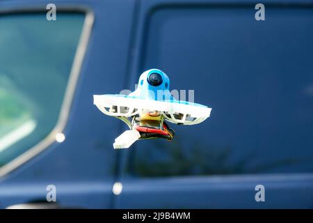 Kleine Drohne blau auch Rennen Quad, mit schützenden Gondel in weiß mit einem blauen Himmel, ein blaues Auto im Hintergrund. Von unten fotografiert. Deutschland. Stockfoto