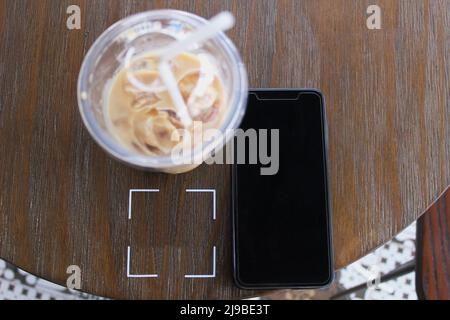 Modell des Telefonbildschirms und ein Glas kalten Kaffee, der jederzeit und überall getrunken werden kann Stockfoto