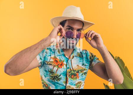 Bärtiger Mann in Sommerkleidung, der seine neuen, modernen, violetten Gläser auf einem isolierten orangefarbenen Hintergrund aufsetzt. Hochwertige Fotos Stockfoto