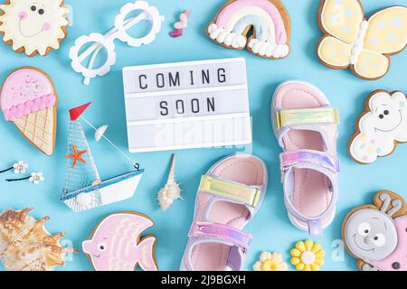 Demnächst verfügbar. Motivationszitat auf Leuchtkasten und niedlichen Sommer-Symbolen auf blauem Hintergrund. Draufsicht, Flat Lay. Kreatives, inspirierendes Sommerkonzept. Stockfoto