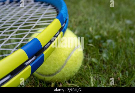 Nahaufnahme ausgewählter Fokus des leichten High-Tech-Tennisschlägers mit synthetischen Darmsaiten und Tennisball auf einem Rasen Stockfoto