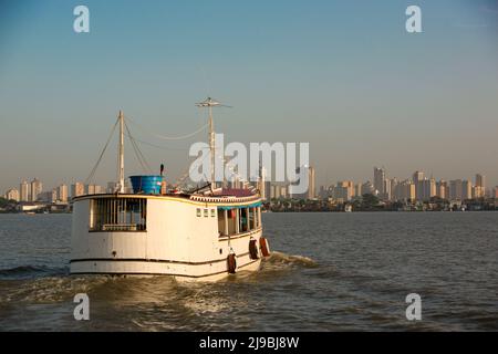 Blick auf den Sonnenaufgang am Flussufer auf die Skyline von Belém do Pará, mit einer kleinen Fähre im Vordergrund, die von den Combu-Inseln zurückfährt. Januar 2008. Stockfoto