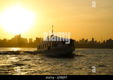 Blick auf den Sonnenaufgang am Flussufer auf die Skyline von Belém do Pará, mit einer kleinen Fähre im Vordergrund, die von den Combu-Inseln zurückfährt. Januar 2008. Stockfoto