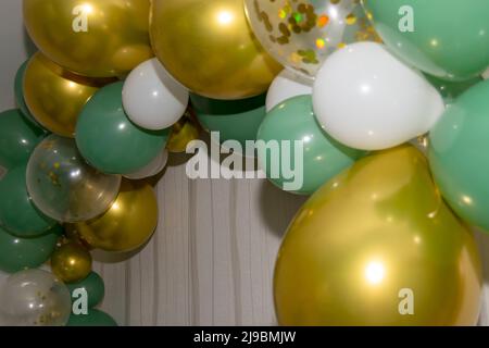 Goldene grüne und weiße Luftballons, die an einer Wand, bei Partys oder Veranstaltungen hängen. Geburtstagsfeier. Stockfoto