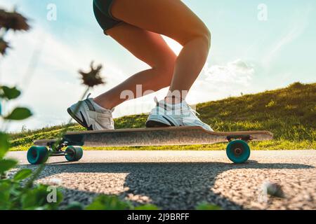 Weitwinkelbeine auf einem Skateschwein oder Longboard in Bewegung an sonnigen Tagen auf der Asphaltstraße. Nahaufnahme eines sich drehenden Rades. Stockfoto