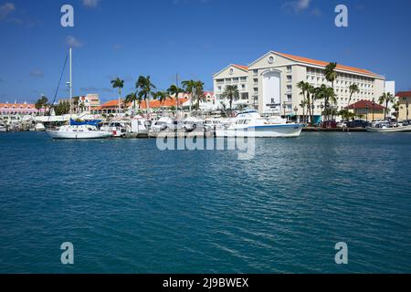 ORANJESTAD, ARUBA - 20. DEZEMBER 2020: Fischerboote und Segelboot im Hafen und im Renaissance Resort dahinter in Oranjestad, Aruba Stockfoto