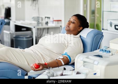 Porträt einer jungen afroamerikanischen Frau, die Blut spendet, während sie im Plasma-Spendenzentrum auf einem Stuhl liegt Stockfoto
