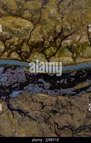 Eine Luftaufnahme zeigt eine Straße, die durch atemberaubende texturierte Landschaften auf den Färöer Inseln führt. Stockfoto