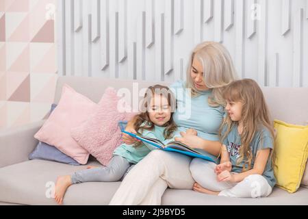 Lächelnde kaukasische Mutter lehrt Töchter, die auf dem Sofa im Wohnzimmer sitzen Stockfoto