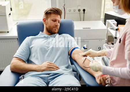 Porträt eines hübschen jungen Mannes, der sich im Zentrum von Med auf die Blutspende vorbereitet, wobei die Krankenschwester hilft Stockfoto