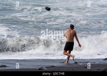 Ein nicht identifizierter Erwachsener spielt mit kaltem ozeanischem Wasser und Steinen, die am schwarzen Lavastrand auf der Insel La Palma, Kanarische Inseln, Spanien, springen Stockfoto