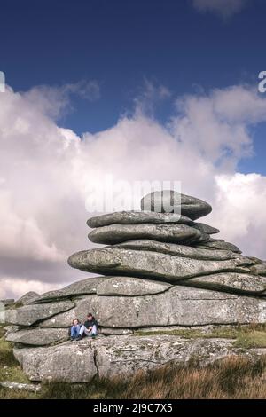 Ein junges Paar, das sich unter einem hoch aufragenden Granitfelsen-Stapel auf dem Stowes Hill auf Bodmin Moor in Cornwall entspannt. Stockfoto