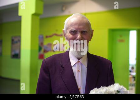 Der alte Mann hält Blumen in der Hand und lächelt. Ein Mann, der 90 Jahre alt ist. Großvater freut sich nach Glückwünschen zu seinem Jahrestag. Das graue h Stockfoto