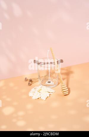 Duftkerze aus biologischem Sojawachs, Docht in einem weißen Keramikglas auf einem beige-rosa Hintergrund. Trendy diy, handgemachtes Konzept. Minimalismus. Isometrische Projektion Stockfoto