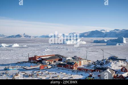 Der Hafen von Uummannaq mit Eisbergen, die im Hintergrund im Meereis eingefroren sind. Stockfoto