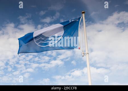 Die prestigeträchtige Blaue Flagge fliegt an einem windigen Frühlingstag am Mundesley Beach in North Nofolk, Großbritannien Stockfoto