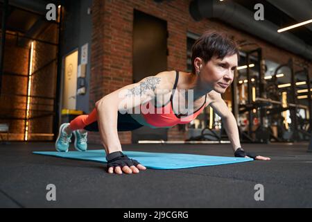 Muskulöse Frau, die Liegestütze auf dem Boden des Fitnessraums ausführt Stockfoto