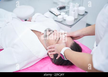 Bärtiger Mann, der im Schönheitssalon eine Gesichtsmassage erhält, oben Stockfoto