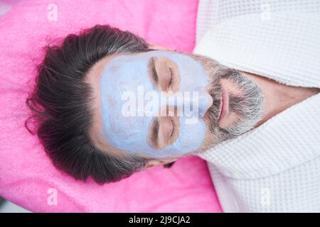 Kaukasischer Mann mit Tonmaske auf seinem Gesicht im Schönheitssalon Stockfoto
