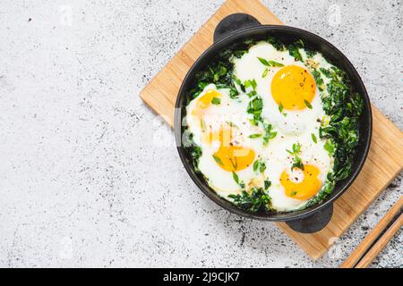 Grüne Shakshuka in einer gusseisernen Pfanne. Spiegeleier mit Spinat und gebratenem Toast. Gesundes, nahrhaftes Frühstück, Stockfoto