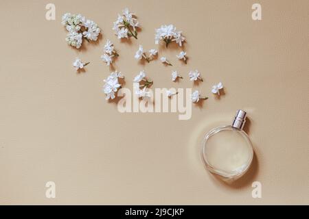 Parfümerie und florale Duft Konzept. Stilvolle Flasche Parfüm mit Spray von Fliederblüten auf beigem Hintergrund. Kreative trendige flach Lay mit Platz für Stockfoto