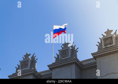 Russische Flagge. Staatsflagge der Russischen Föderation gegen den blauen Himmel. Das Banner des Landes auf dem Gebäude. Stockfoto