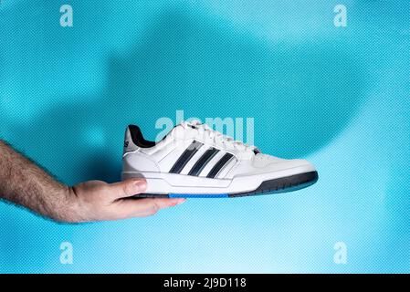 Belgrad, Serbien - 11. Mai 2022. Hände mit neuen Adidas Tennisschuhen auf blauem Hintergrund. Neue Adidas Sneakers oder Sportschuhe - Herren Sportschuhe. Pai Stockfoto