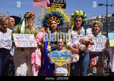 London, England, Großbritannien. 22.. Mai 2022. Demonstranten, die traditionelle Blumenhedressen tragen, und zwei mit eingewickelten Stoffen, die mit Blut bedeckten Babys ähneln, versammeln sich am Marble Arch. Menschenmengen marschierten vom Hyde Park zur russischen Botschaft in London und riefen die internationale Gemeinschaft dazu auf, zur Rettung der Kinder in der Ukraine beizutragen, und protestierten gegen die Gräueltaten, die angeblich von russischen Truppen begangen wurden. (Bild: © Vuk Valcic/ZUMA Press Wire) Stockfoto