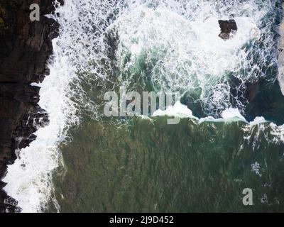 Nahaufnahme. Die Meeresschaumwelle schlägt gegen einen großen Felsbrocken am Ufer. Die Größe und Schönheit der Natur, natürliche Elemente, Gefahr, Schönheit des Natu Stockfoto