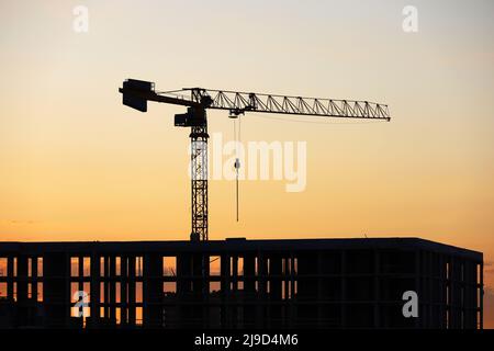 Silhouette eines Turmdrehkrans über dem unfertigen Gebäude bei Sonnenaufgang. Wohnungsbau, Wohnblock in der Stadt auf dem Hintergrund Stockfoto