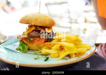 Rustikaler Gourmet-Hamburger mit dicken pommes frites sevisa im Terrassenrestaurant am Tag Stockfoto