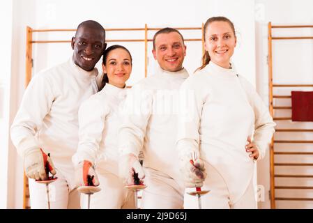 Gruppe positiver Fechter, die beim Fechttraining mit Folien zusammen stehen Stockfoto