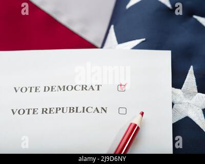 Ein Häkchen auf dem Stimmzettel gegen einen Demokraten und ein roter Bleistift vor dem Hintergrund der amerikanischen Nationalflagge. Nahaufnahme. Wahlen, Wahlen, die Stockfoto