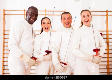 Gruppe positiver Fechter, die beim Fechttraining mit Folien zusammen stehen Stockfoto