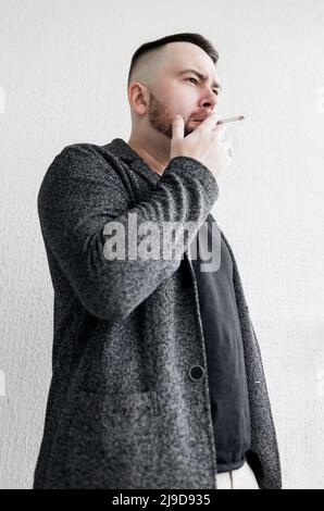 Junger bärtiger Mann raucht Zigarette. Guy süchtig Nikotin von Zigaretten . Er raucht draußen in der Öffentlichkeit Zigarette. Stockfoto