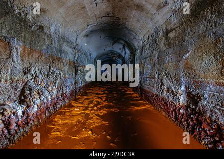 Dunkler, schmutziger, überfluteter, gewölbter Betonentwässerungsminentunnel Stockfoto