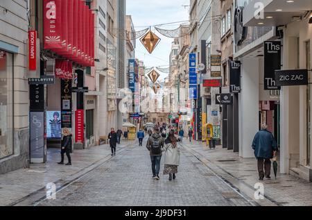 Athen, Griechenland - Februar 13 2022: Zufällige Menschen auf der Ermou-Straße, mit der byzantinischen Kirche Panaghia Kapnikarea im Hintergrund. Stockfoto