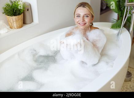 Porträt einer jungen blonden hübschen Frau, die lächelt und Blasen in der Badewanne genießt. Stockfoto