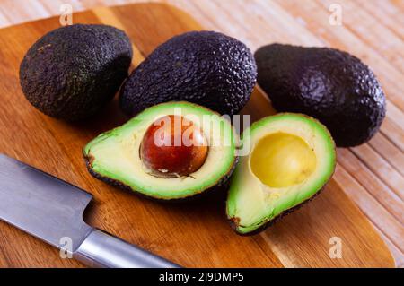 Ganze und halbierte Avocados auf Holzhintergrund Stockfoto