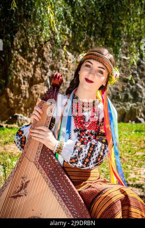 Ukrainischer Musiker in authentischer Nationaltracht sitzt an einem Felsen. Ukrainische Frau mit einem Bandura-Musikinstrument, bevor sie Volksmusik aufführt Stockfoto