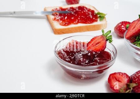 Toast mit Erdbeermarmelade zum Frühstück auf weißem Hintergrund. Draufsicht. Frische Erdbeeren und hausgemachte Erdbeermarmelade reifen, auf Brot verteilen. Stockfoto