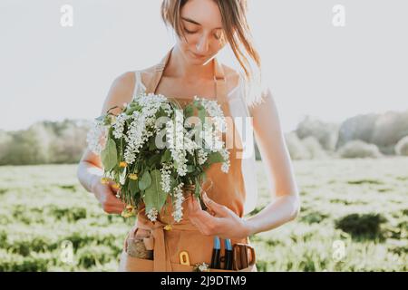 Portrait einer schönen Frau, die auf dem blühenden Feld einen Strauß von wilden Blumen macht. Sommer-Lifestyle, Naturliebhaber und Freiheitskonzept. Floristen-Workshop und Stockfoto
