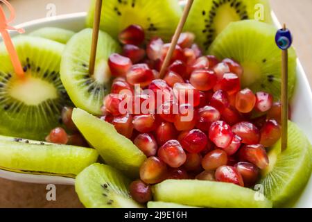 In Scheiben geschnittene Kiwi- und Granatapfelkerne auf einem Teller, Obstsalat Stockfoto