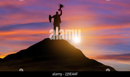 Silhouette Sieg Geschäftsmann mit Trophäe kletterte auf die Spitze des Berges über den Himmel und Sonnenlicht Hintergrund. Erfolg, Zielerreichung, Führung. Stockfoto