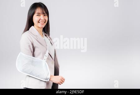 Arm gebrochen. Geschäftsfrau zuversichtlich lächelnd gebrochenen Arm nach Unfall und tragen Armschiene für die Behandlung, aufgeregt glücklich asiatische weibliche Sling Unterstützung han Stockfoto