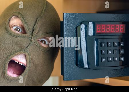 Ein fröhlicher Mann in einer Maske feiert den Erfolg, indem er einen Safe auf einem numerischen Code öffnet Stockfoto