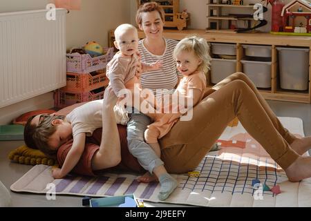 Glücklicher Vater mit kleinen Kindern, die zu Hause spielen. Papa Mutter kuschelt mit Kindern und hält sie an den Händen. Spaß in der großen Familie, sonniger Tag. DVDAD Carry Stockfoto