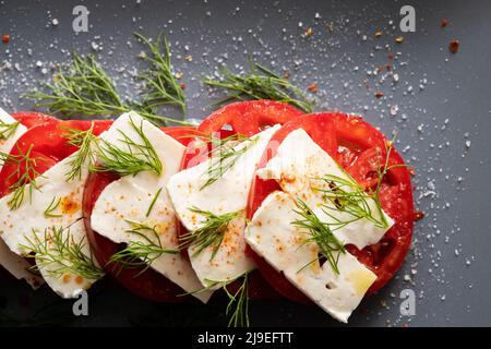 Hausgemachter Käse mit Tomaten und Dill auf einem grauen Teller. Vorspeisen für den Tisch und Wein. Vorderansicht. Stockfoto