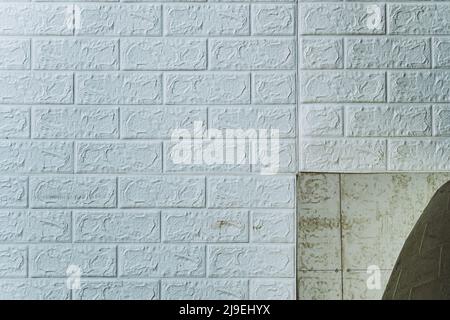 Die Tapete beginnt sich abzulösen. Die Tapete aus alten weißen Ziegeln schälte sich von der Wand im Raum, weil es feucht war oder sich nicht gut klebte. Reparieren Sie A Stockfoto