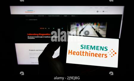 Person, die Mobiltelefon mit Logo der deutschen Siemens Healthineers AG auf dem Bildschirm vor der Business-Webseite hält. Konzentrieren Sie sich auf die Telefonanzeige. Stockfoto